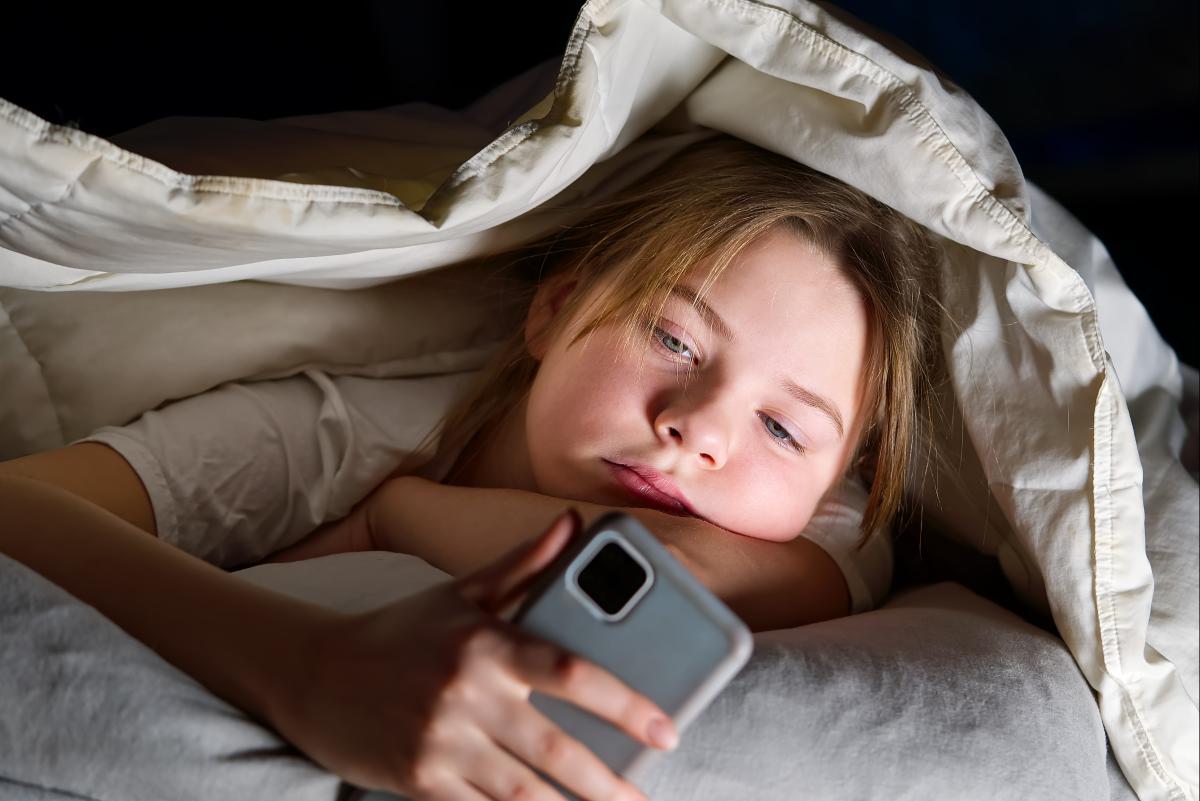 Junges Mädchen schaut nachts unter ihrer Bettdecke auf ihr Smartphone