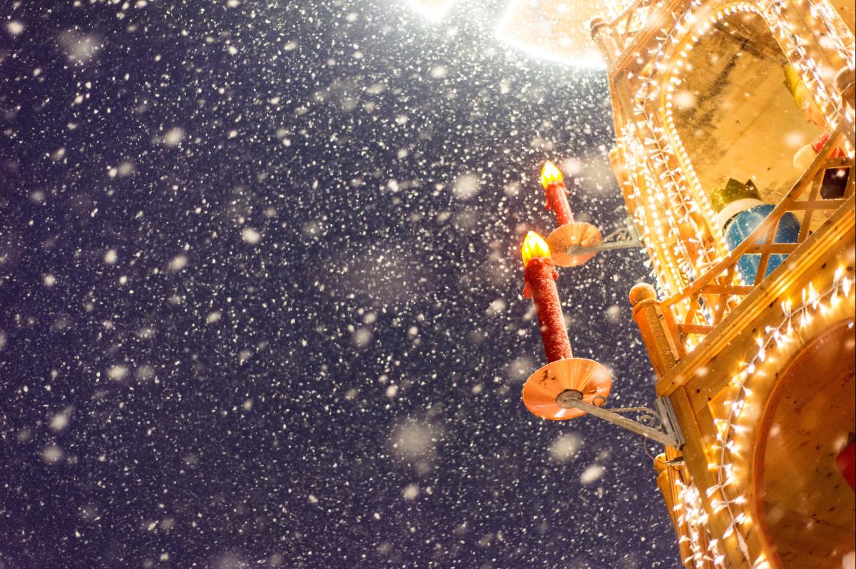Ausschnitt eines Adventsbogens mit Kerzen und Schneefall bei Dämmerung