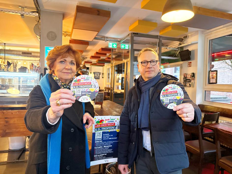 Die Opferschutzbeauftragte Barbara Havliza und Minister Dr. Limbach zeigen Bierdeckel mit Informationen zu K.O.-Tropfen Missbrauch