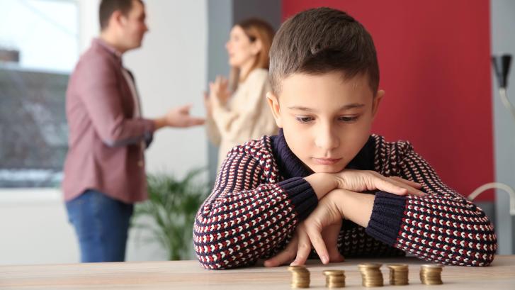 Kind zählt Geld, im Hintergrund streiten die Eltern