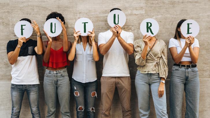 Gruppe von sechs nebeneinander stehender Menschen hält Buchstaben in die Luft, die das Wort Future bilden.