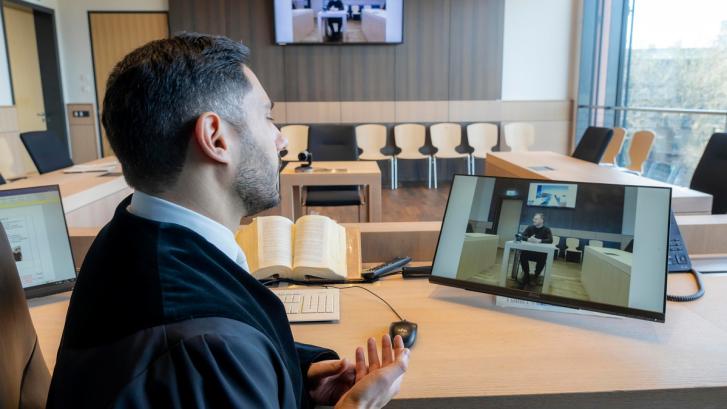 Mann in Robe im Gerichtssaal vor Bildschirm