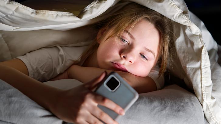 Junges Mädchen schaut nachts unter ihrer Bettdecke auf ihr Smartphone