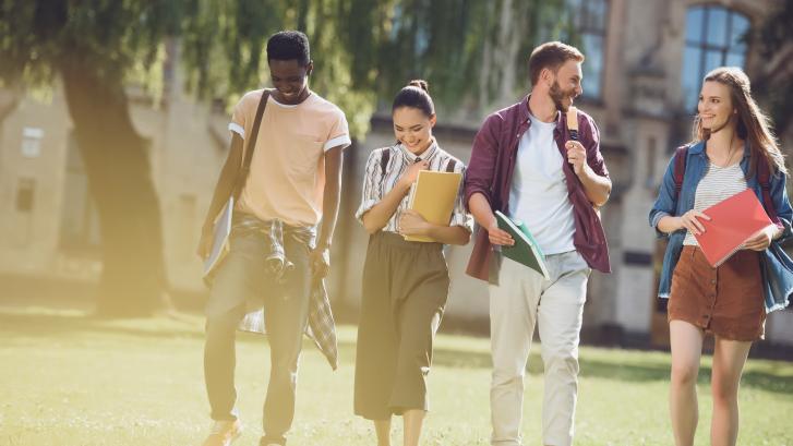 Eine Gruppe von vier jungen diversen Studierenden, die über den Uni-Campus spazieren