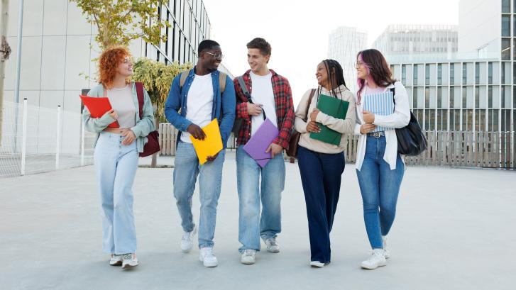 Diverse Gruppe mit fünf jungen Erwachsenen spaziert lachend über Campus